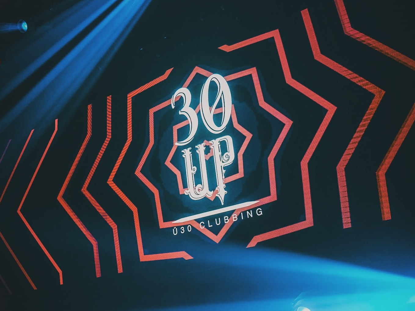 Leuchtendes 30 UP Clubbing Logo auf einer Bühne mit Lichteffekten.