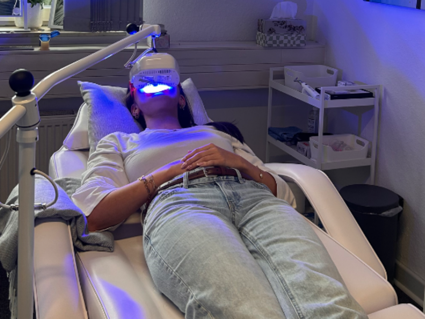 Frau bei kosmetischer Zahnaufhellung mit LED-Licht auf Behandlungsstuhl in moderner Praxis.