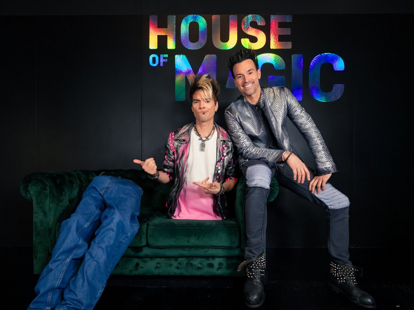 Zwei Männer sitzen auf einem Sofa vor dem Schriftzug „House of Magic“, einer von ihnen scheint keine Beine zu haben.