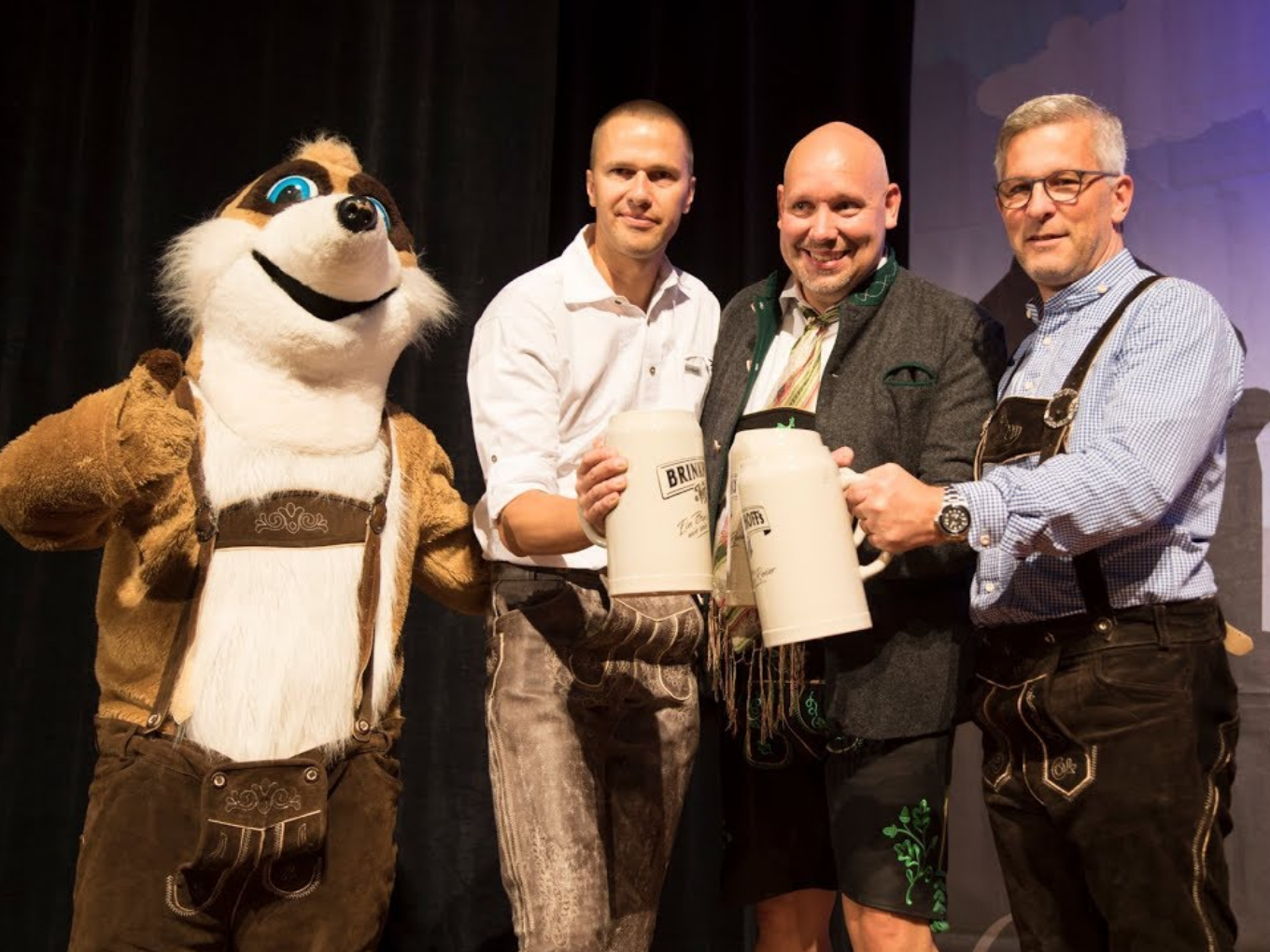 Männer in Tracht und Maskottchen stoßen mit Bierkrügen beim Oktoberfest Hagen an.