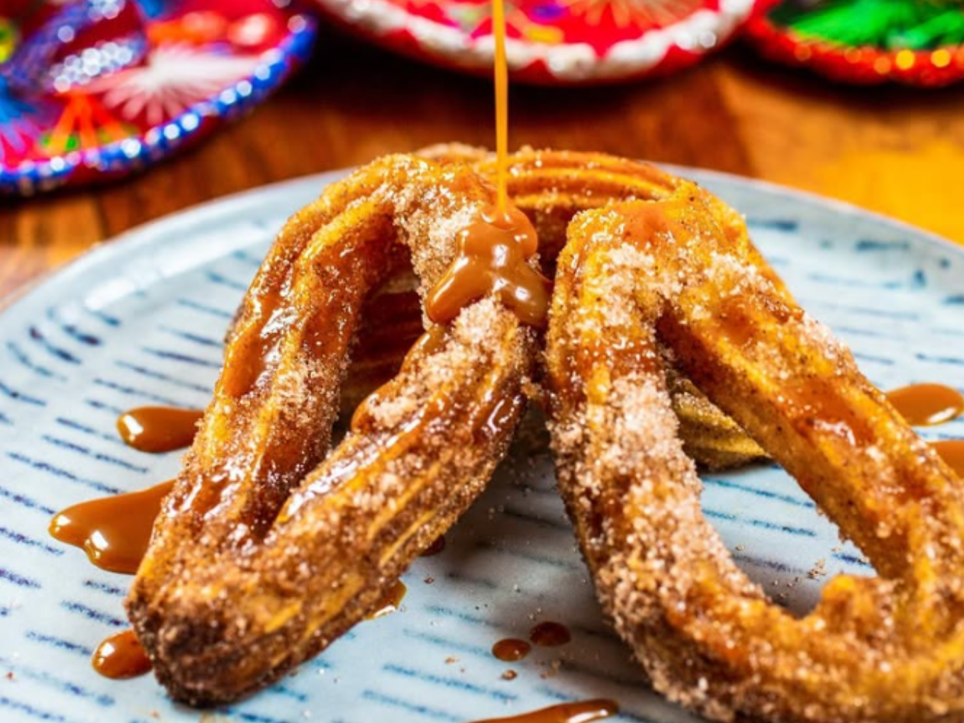 Drei Churros auf einem Teller, mit Karamellsauce übergossen.