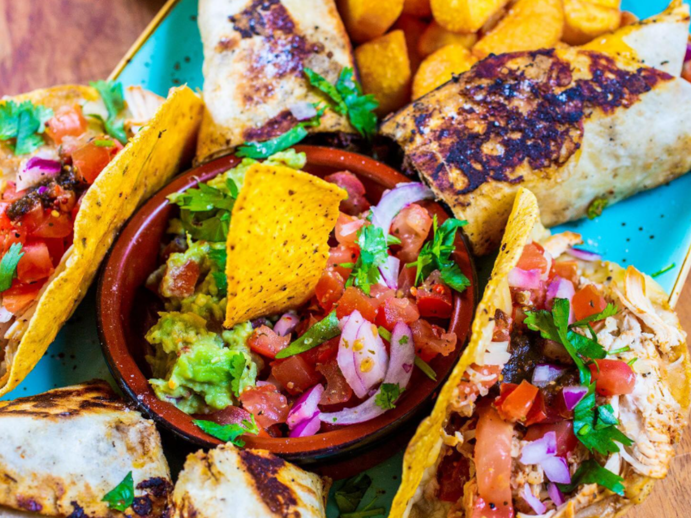 Verschiedene Tacos, Burritos und Guacamole auf einem bunten Teller.