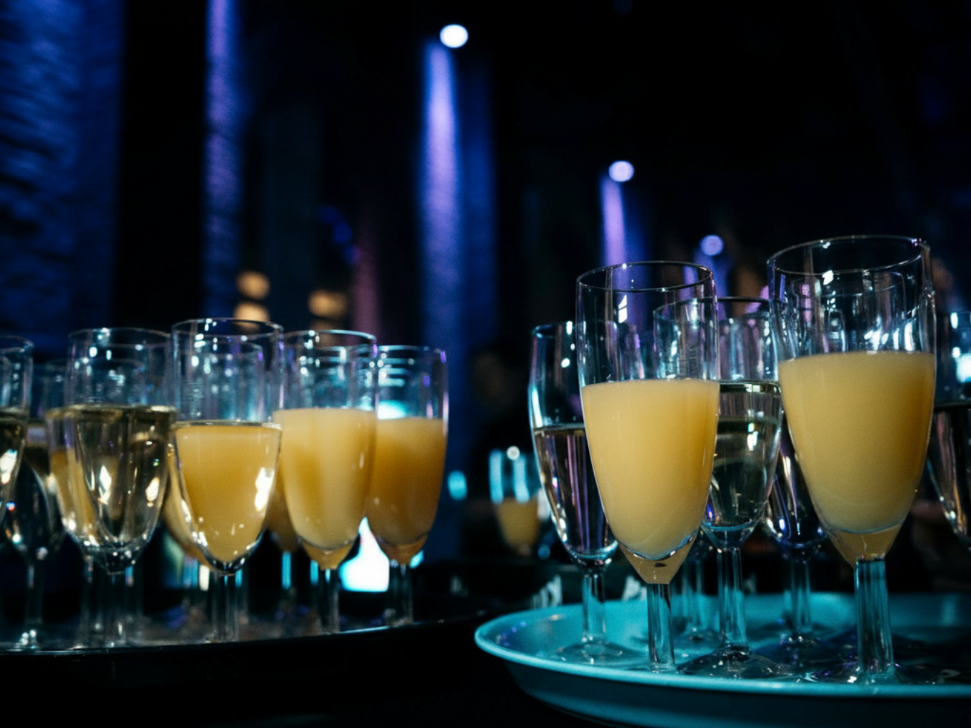 Sekt- und Orangensaftgläser auf Tabletts bei einer Ü30-Party.
