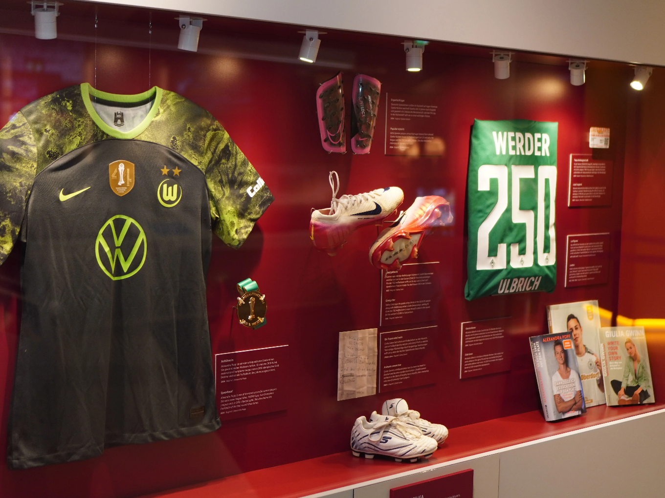 Vitrine mit Fußballtrikot, Sportschuhen, Schienbeinschonern, Medaille und Büchern.