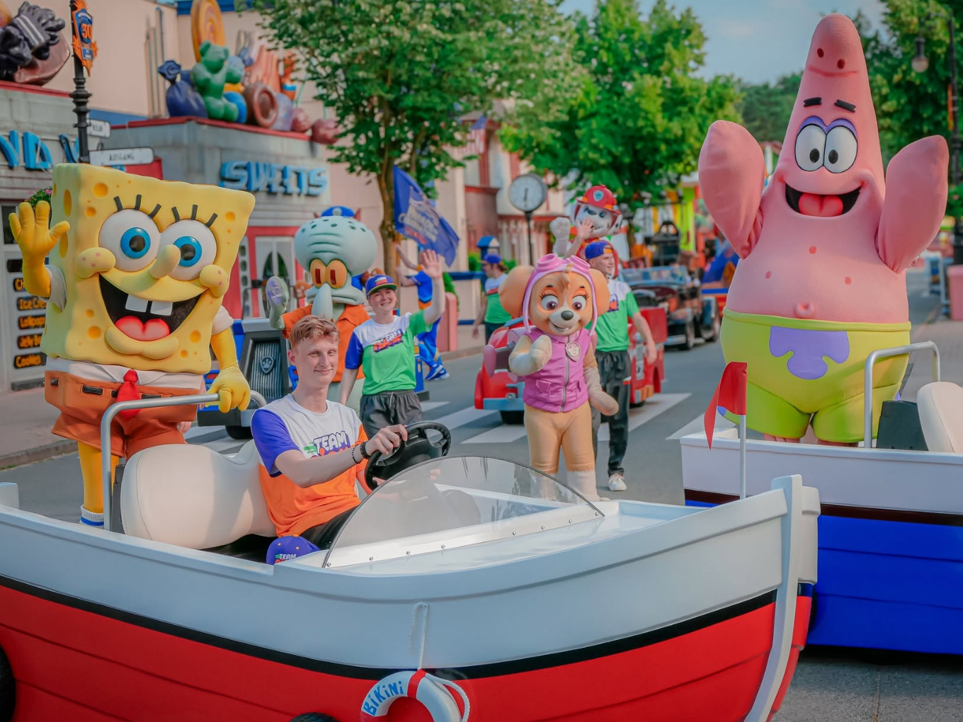 Menschen in Kostümen, darunter SpongeBob und Patrick, fahren in kleinen Booten durch einen Freizeitpark.