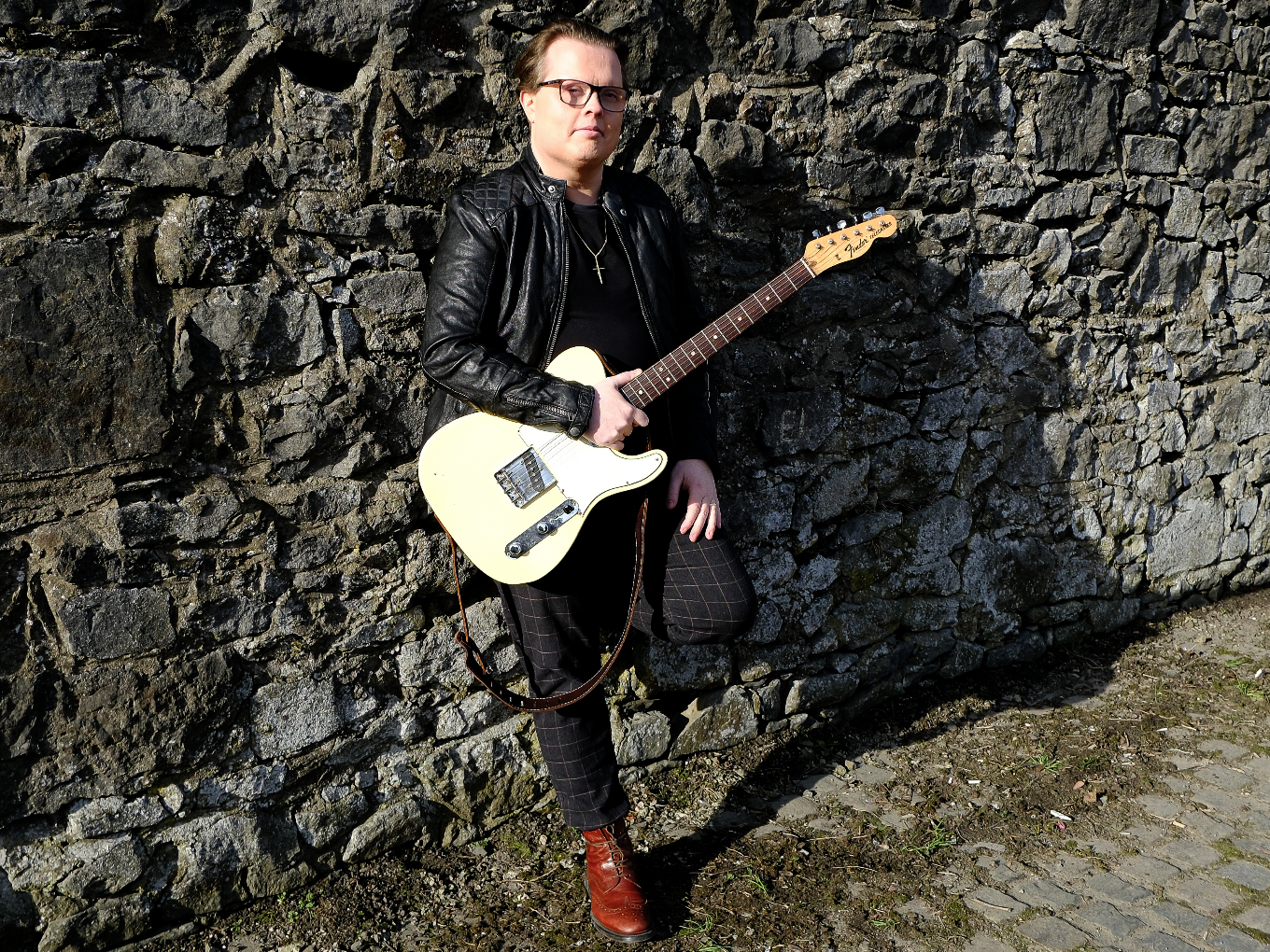 Angelo Kelly mit Gitarre posiert vor Steinwand