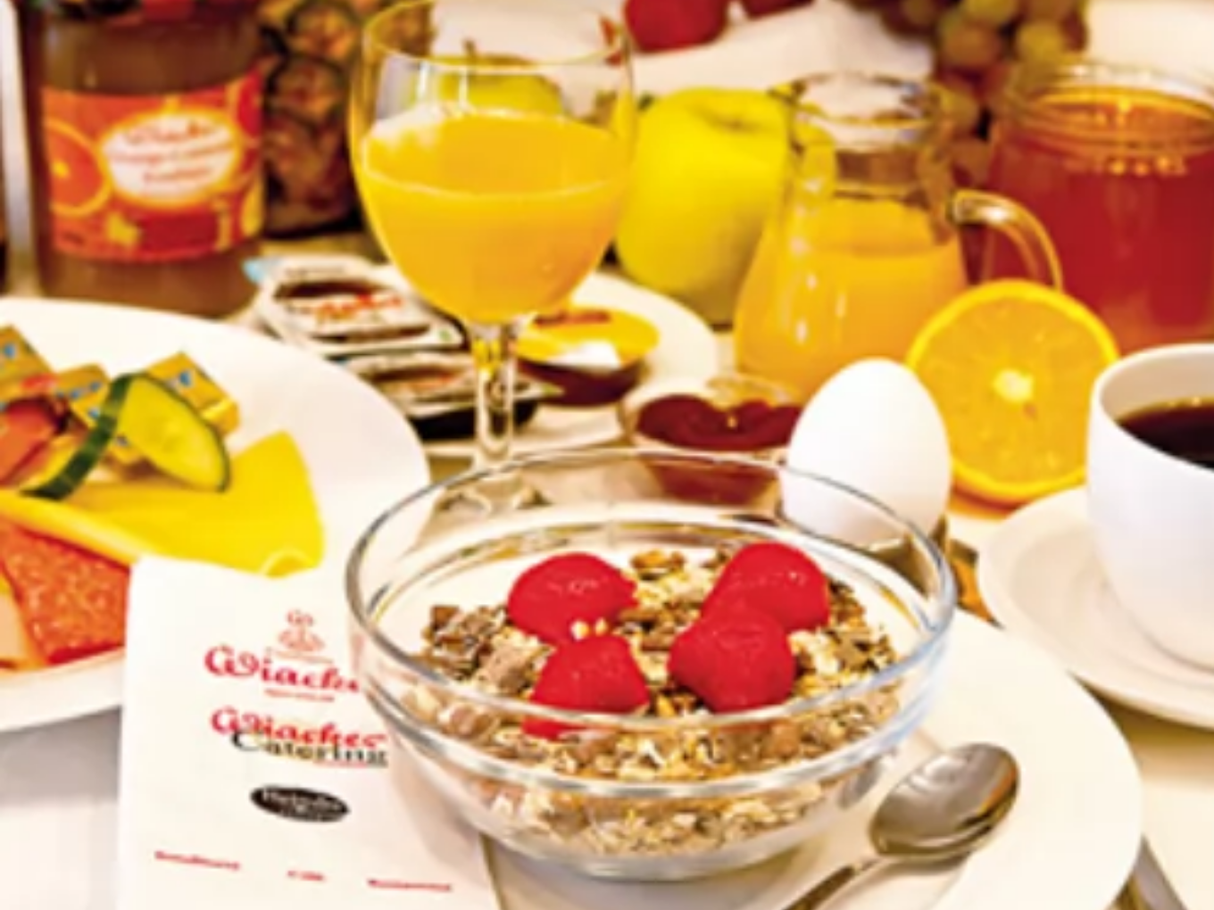 Ein reich gedeckter Frühstückstisch mit Müsli, Himbeeren, gekochtem Ei, Orangensaft, Kaffee, Käse, Wurst, Marmelade und frischem Obst.