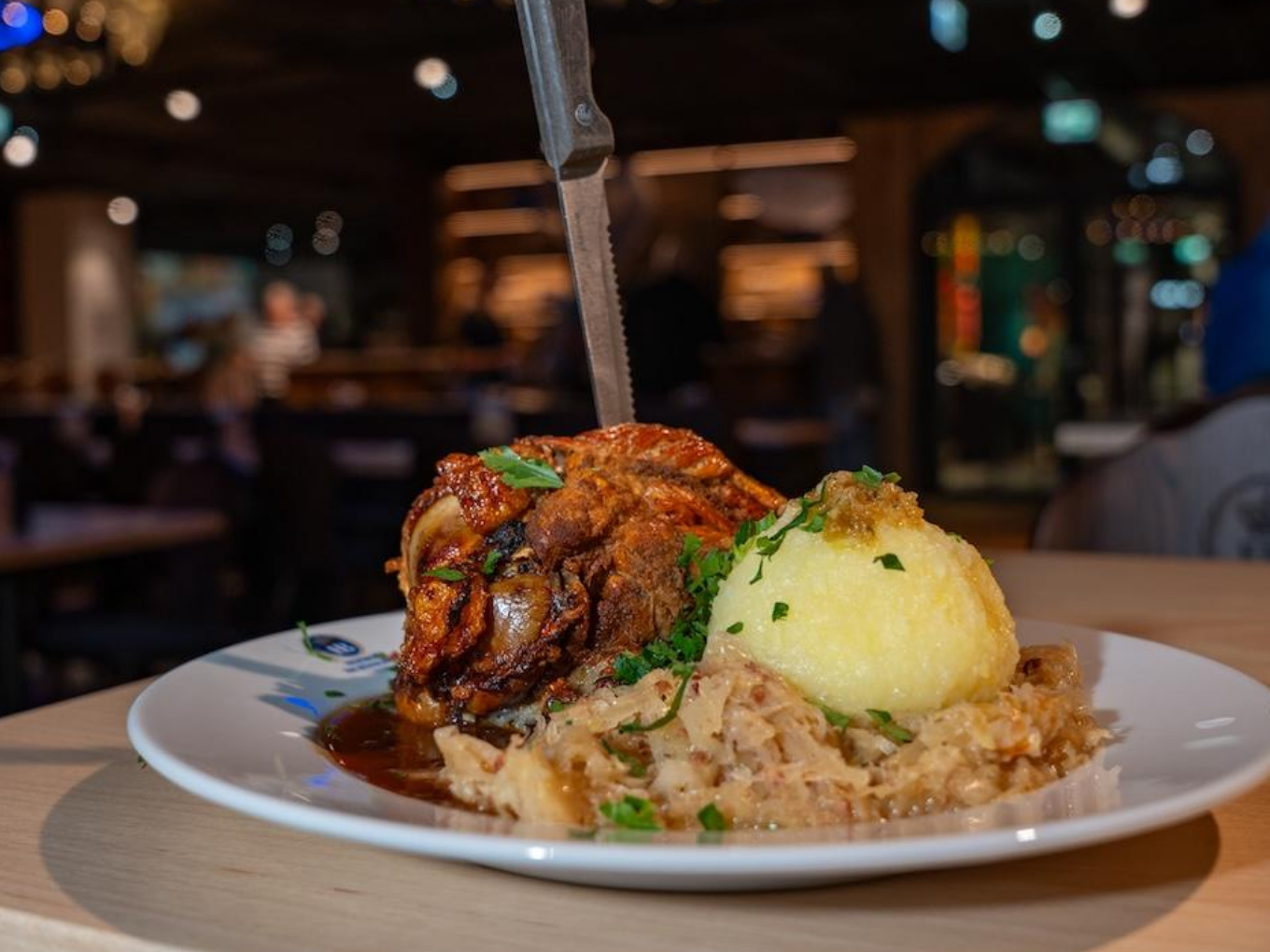 Teller mit Schweinshaxe, Kartoffelknödel und Sauerkraut, im Restaurant serviert.