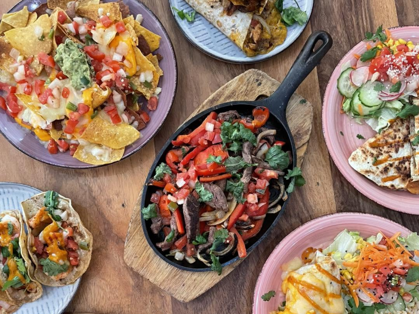 Verschiedene mexikanische Gerichte wie Nachos, Tacos, Quesadillas und Fajitas auf mehreren Tellern.