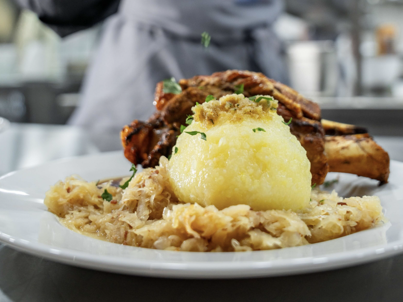 Teller mit Schweinshaxe, Kartoffelknödel und Sauerkraut in einer Restaurantküche.