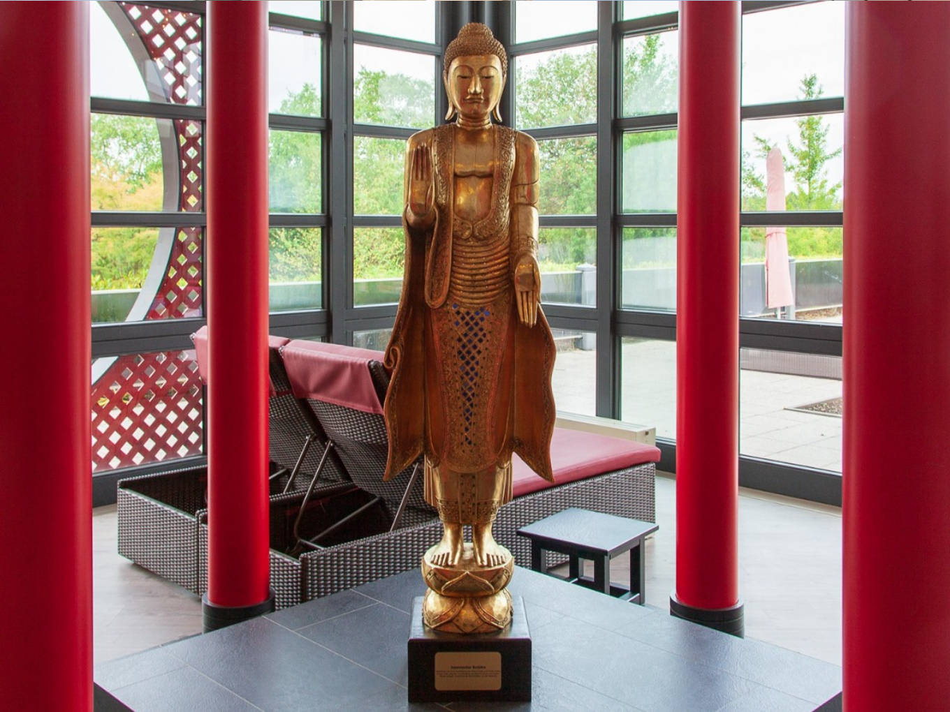 Goldene Buddha-Statue zwischen roten Säulen im asiatisch gestalteten Ruhebereich.