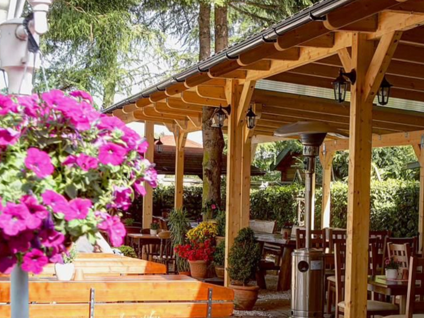Biergarten mit Holzbänken, Tischen und Blumen unter einem Holzdach