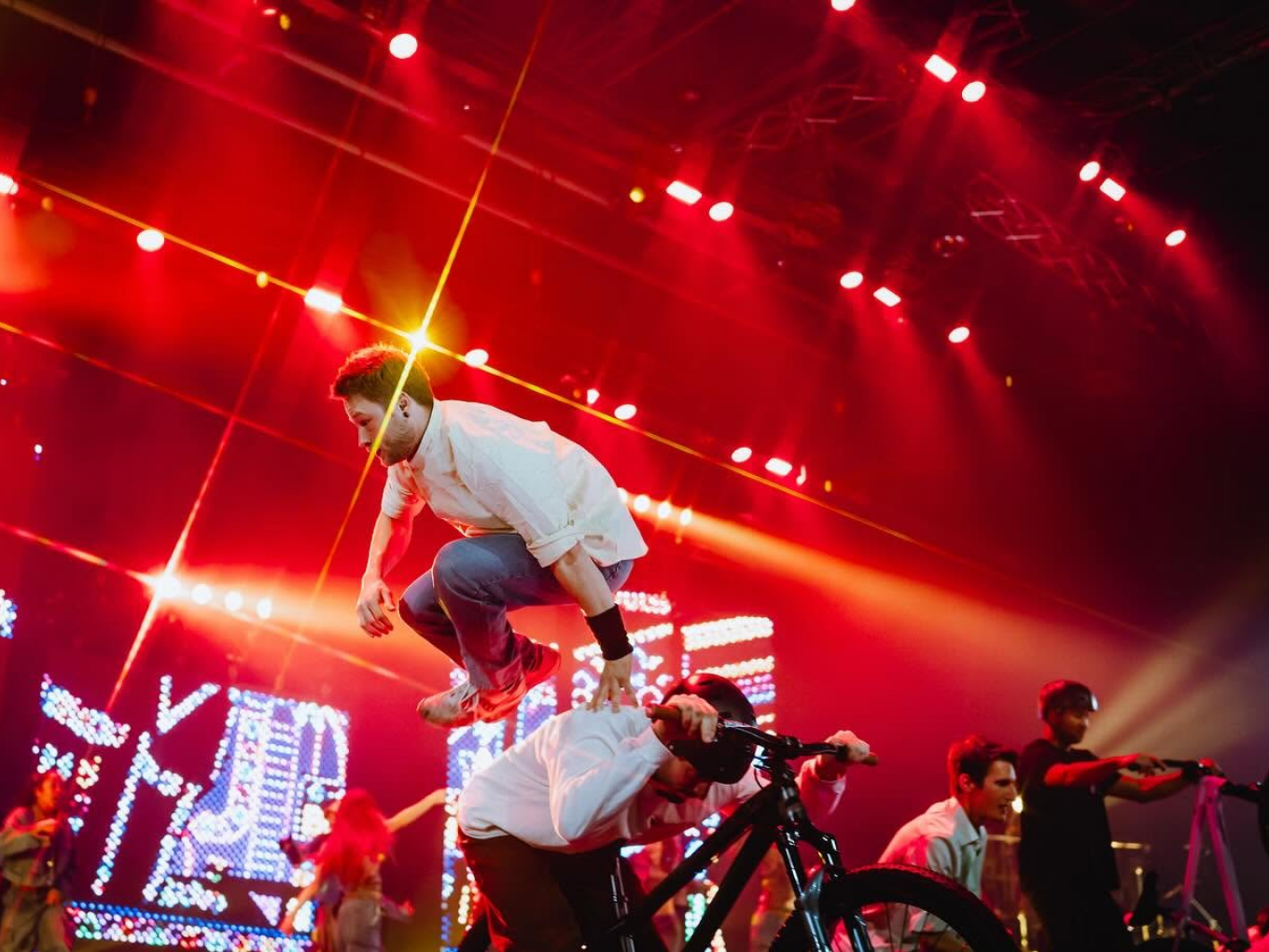 Artist springt über einen BMX-Fahrer, bunte Lichter im Hintergrund.