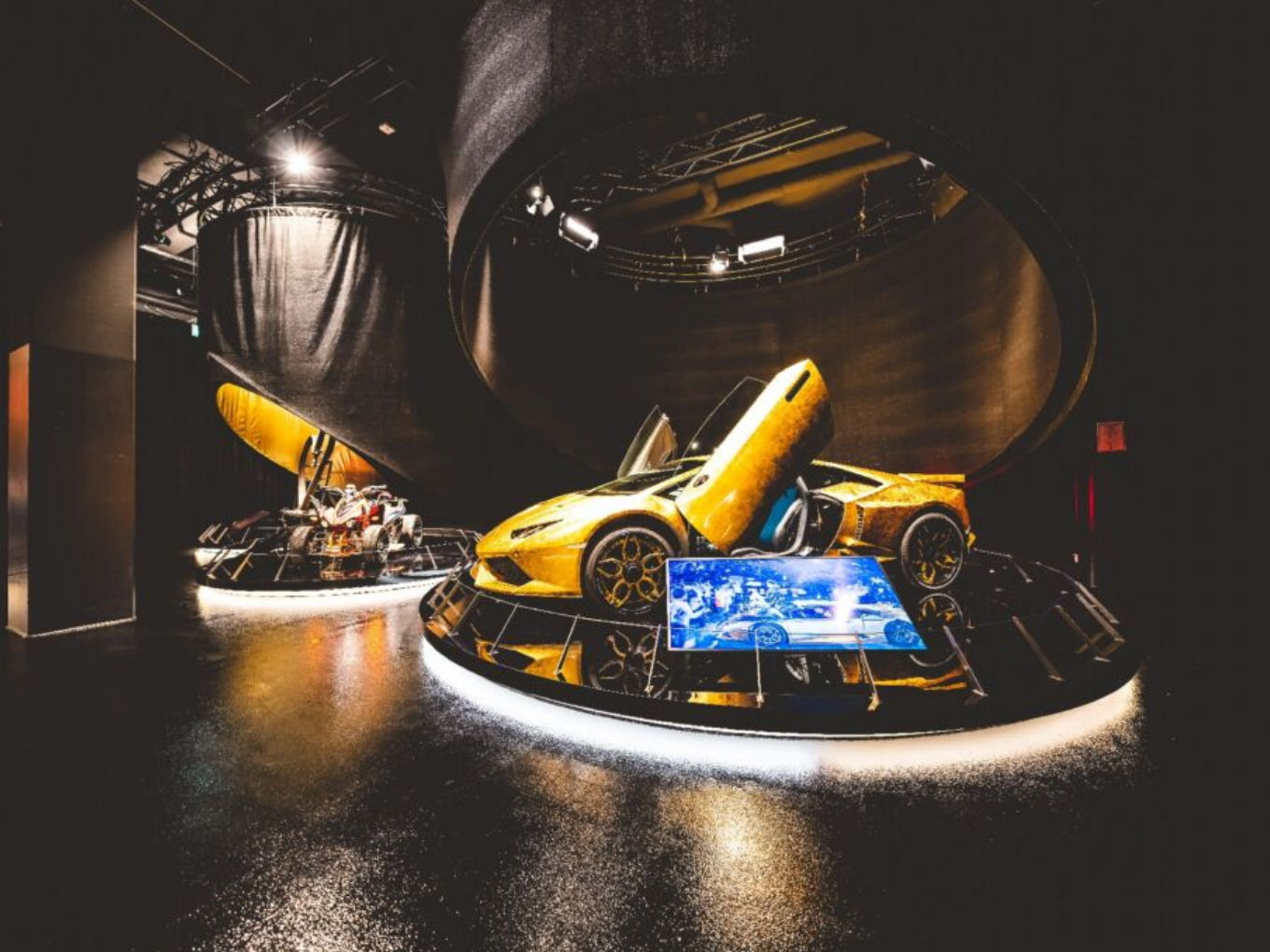 Ein goldfarbenes Auto mit geöffneten Türen steht in einer Ausstellung, daneben ein weiteres Ausstellungsstück.