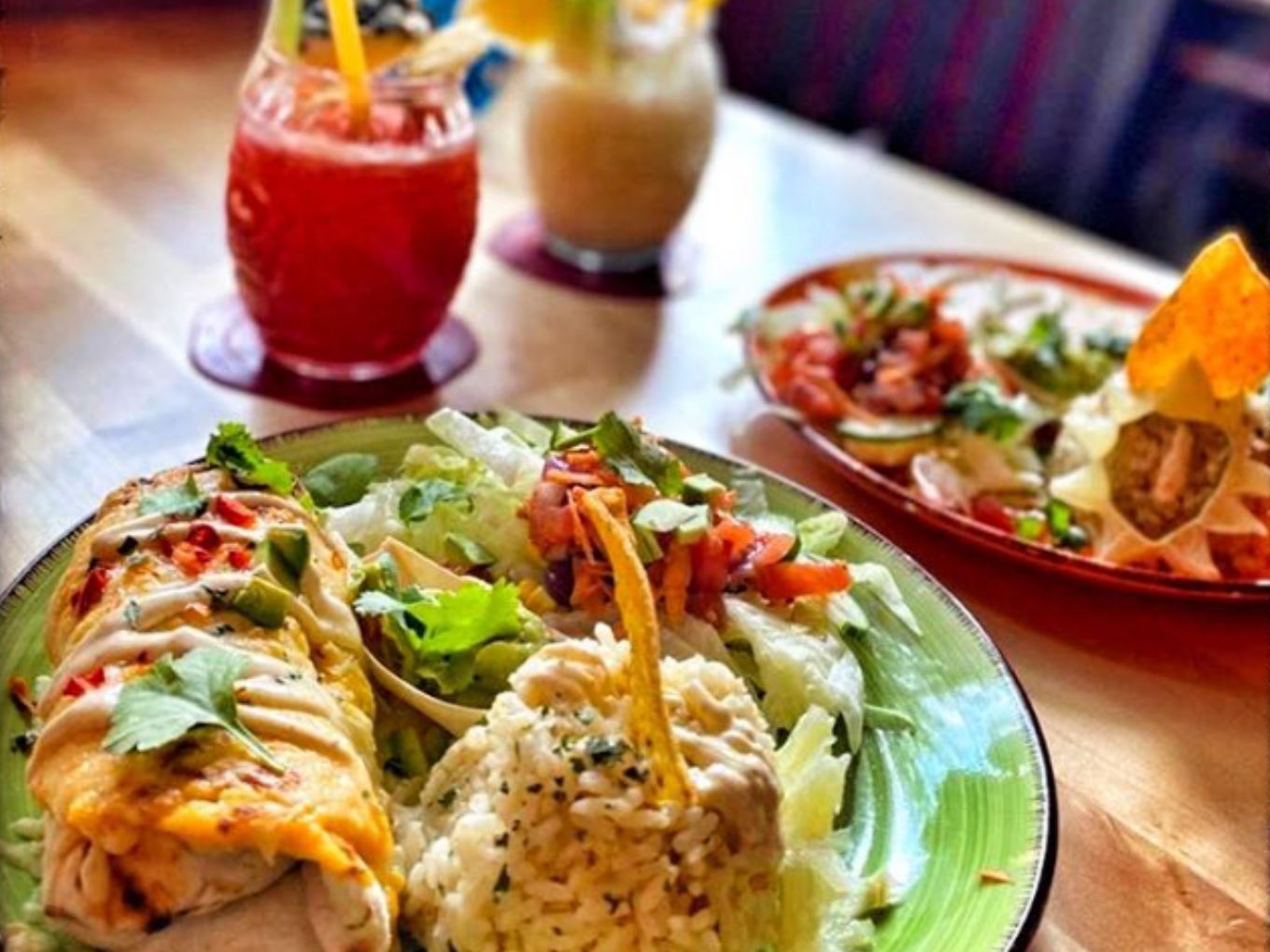 Teller mit Burrito, Reis, Salat und mexikanischen Cocktails im Hintergrund.