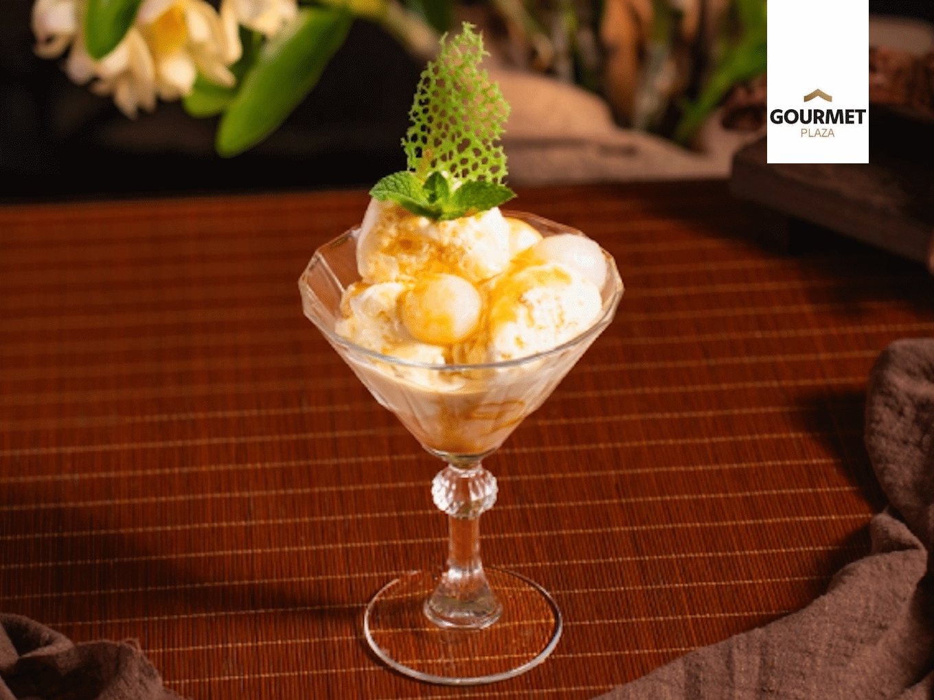 Vanilleeis mit goldener Sauce, Minze und knuspriger Dekoration im Dessertglas.