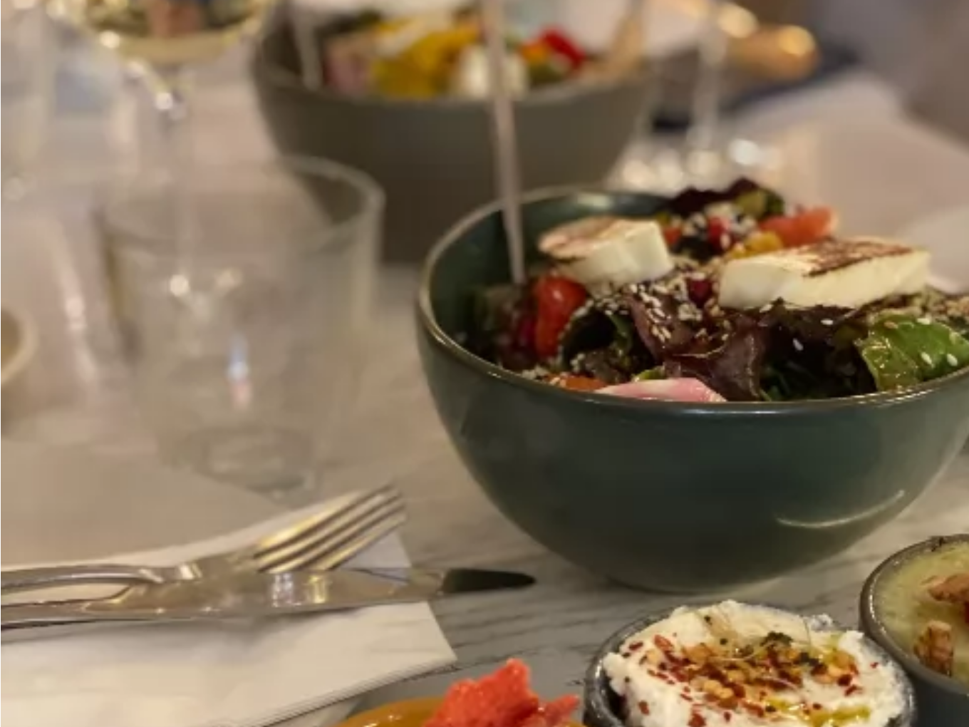 Ein gedeckter Tisch mit einer Schüssel griechischem Salat, darauf Feta und Sesam, daneben weitere kleine Schälchen mit Dips und Vorspeisen.