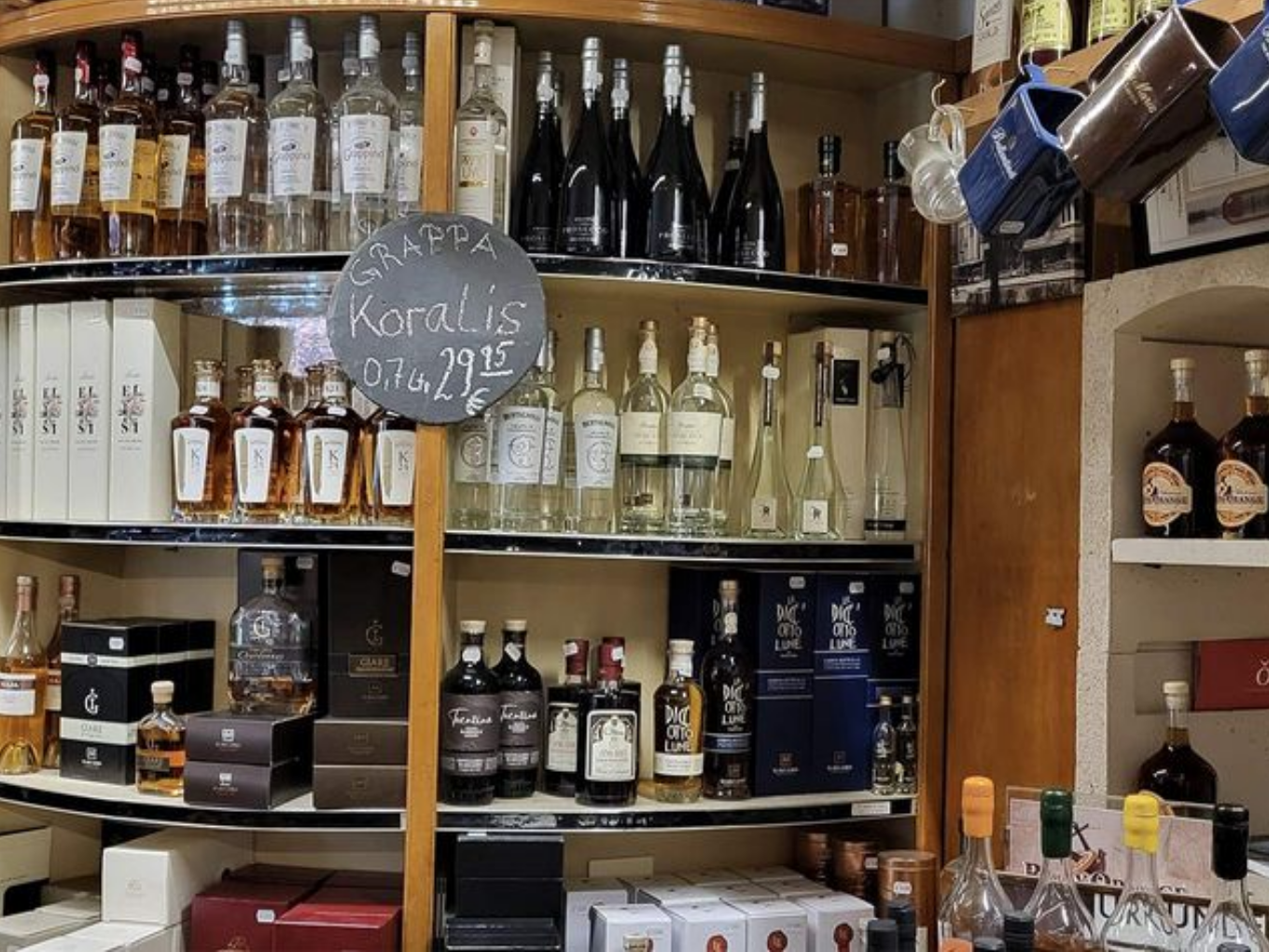 Regal mit Grappa- und Spirituosenflaschen, Preisschild „Grappa Koralis“.