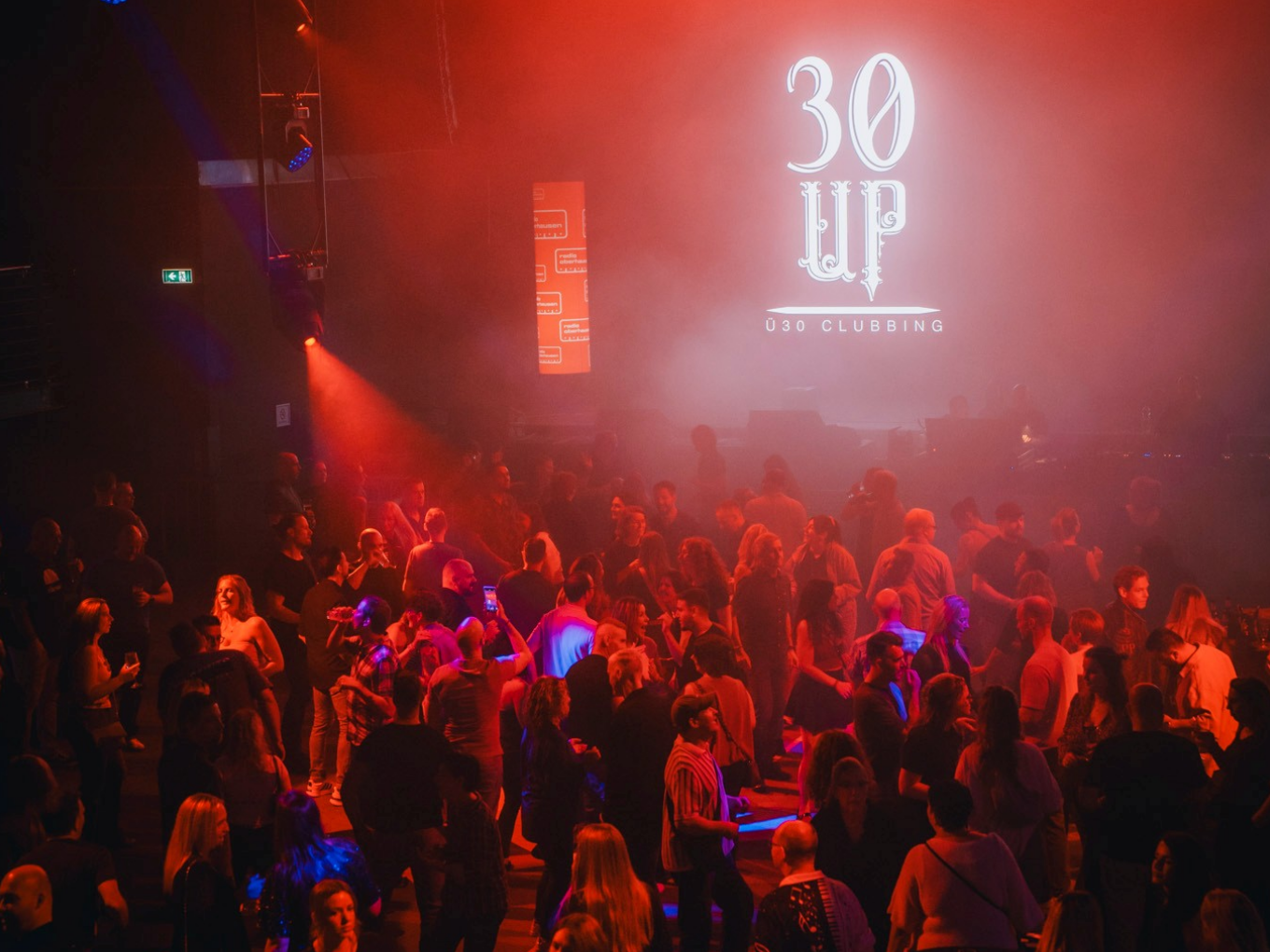 Menschen tanzen bei rotem Licht beim 30 UP Clubbing Event