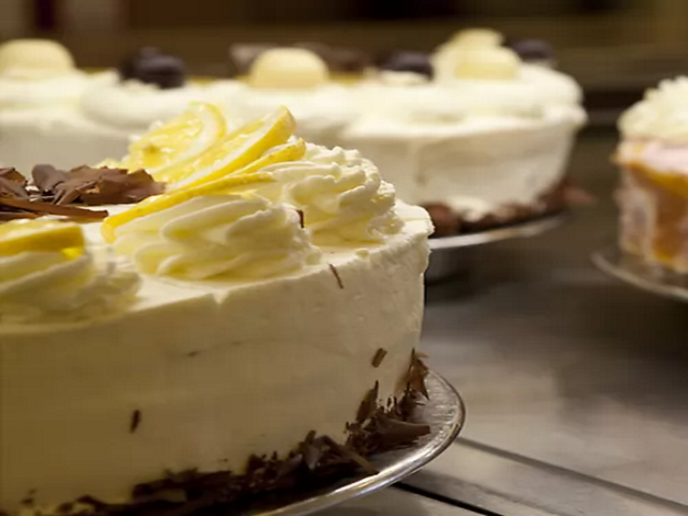 Verschiedene Sahnetorten auf einer Theke, im Vordergrund eine Torte mit Zitronenscheiben und Schokoraspeln dekoriert.
