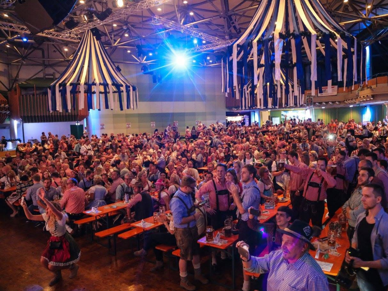 Festsaal der Stadthalle Hagen mit Oktoberfest-Dekoration und vielen Gästen an Bänken.