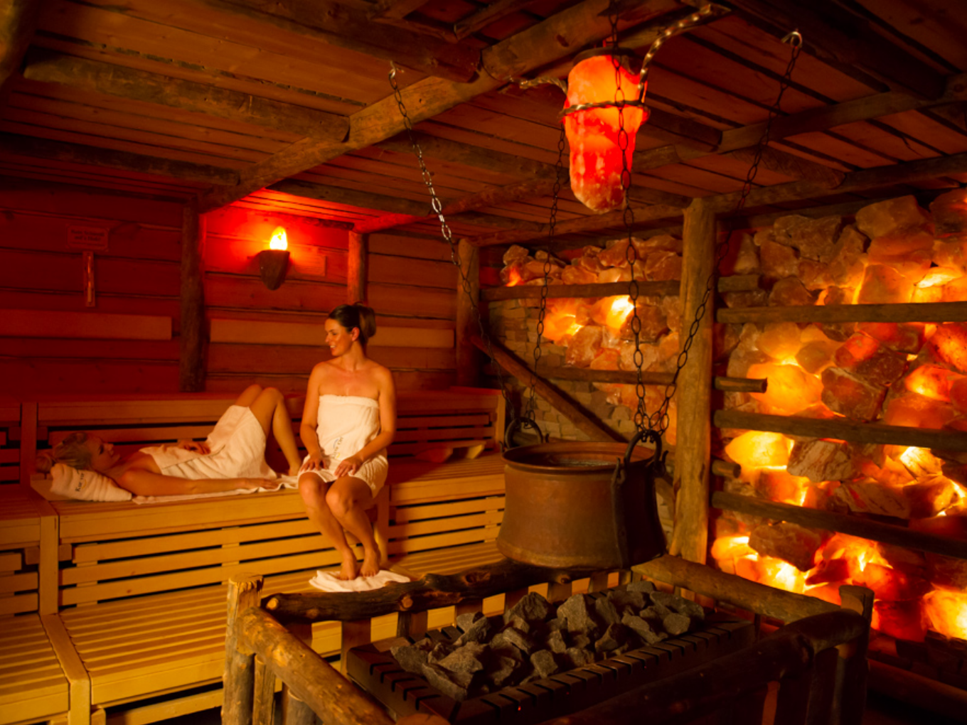Zwei Gäste entspannen in einer rustikalen Sauna mit warm beleuchteten Salzsteinen.