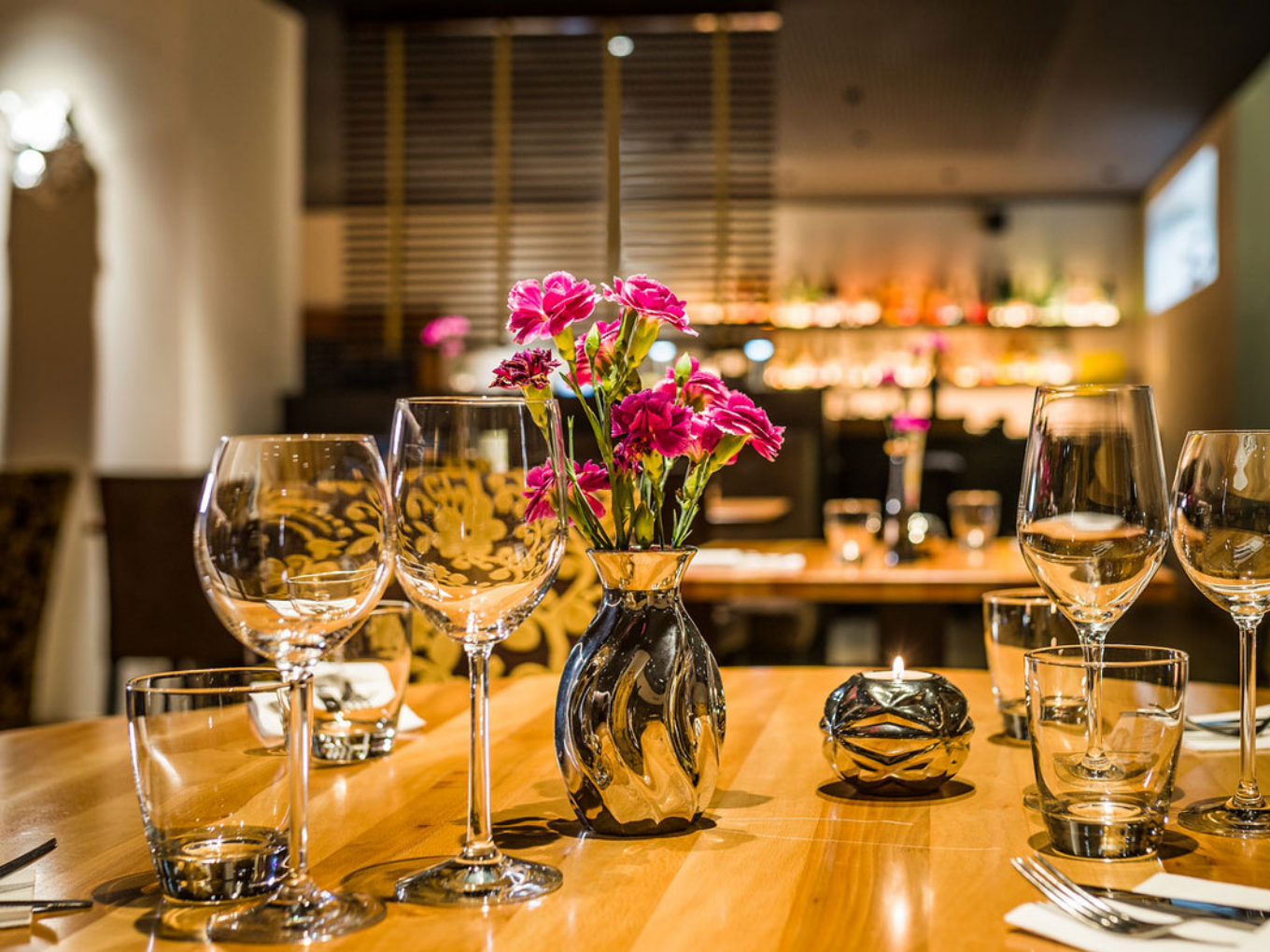 Nahaufnahme eines gedeckten Tisches mit Blumenstrauß und Gläsern in einem Restaurant.