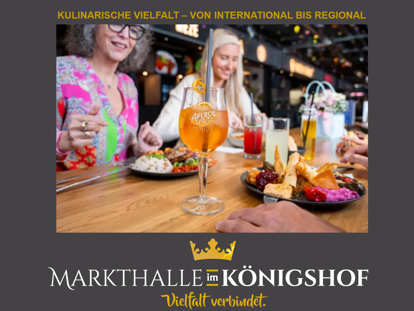 Mehrere Personen essen gemeinsam an einem Tisch in der Markthalle im Königshof, verschiedene Speisen und Getränke stehen bereit.